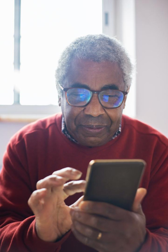 äldre man tittar fokuserat på sin mobiltelefon