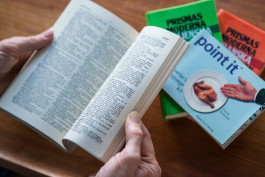 en person läser genom ett lexikon på bordet bakom ligger tre böcker