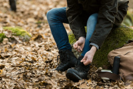 en person sitter på en sten och knyter skorna det är höstlöv på marken