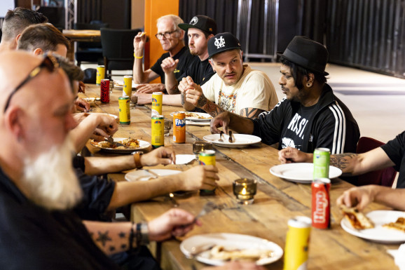 Personer äter vid ett träbord, läskburkar står på bordet