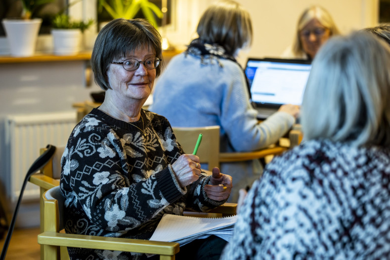 Kvinna i fokus i grupp av andra, hon höjer en penna