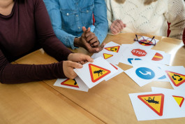 tre personer sitter vid ett bort och tittar på bilder av vägmärken