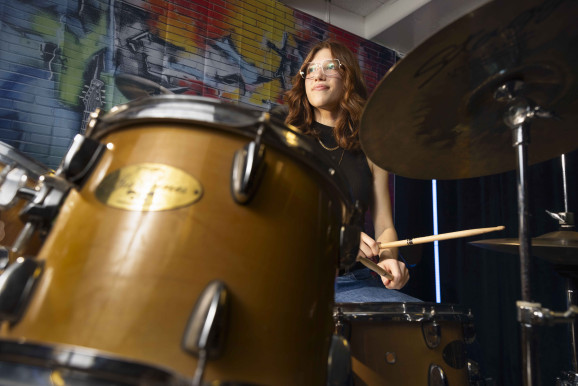 I förgrunden ett trumset, bakom vilket ett ung person sitter redo med trumpinnarna.