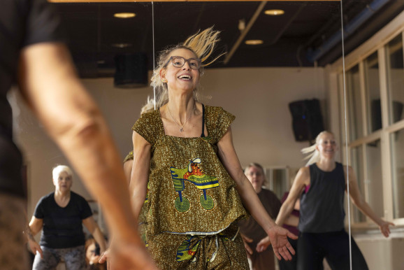 Dansgrupp med flera deltagare. I mitten en glad kvinna i guldglittriga kläder som dansar så håret svänger.
