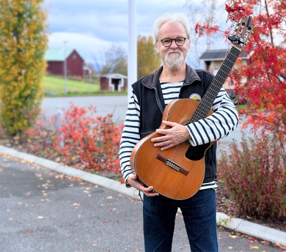 Foto på Anders Hedén utomhus med sin gitarr i famnen