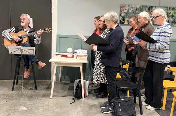 Anders Hedén på sin stol med gitarr och delar av kören i Hackås.