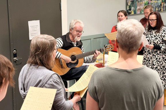 Inzoomad bild på Anders Hedén med sin gitarr tillsammans med sin kör.