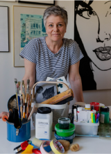 Porträtt av Lena Ailm ståendes bakom en massa hantverksredskap, penslar, med mera!
