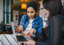två unga kvinnor sitter tillsammans och jobbar på en laptop