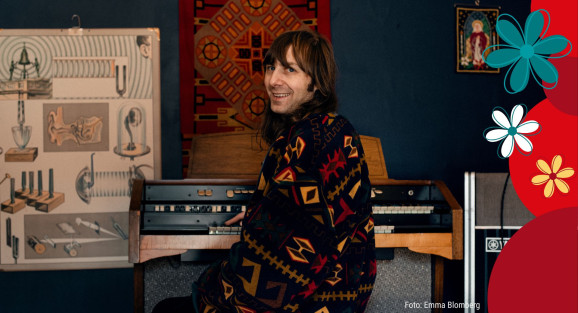 Niklas Eriksson sitter vid ett klaviatur. Han bär en kofta med grafiska mönster i gult och rött. På väggen bakom honom hänger en plansch med ljudillustrationer (stämgaffel, öra m.m.)