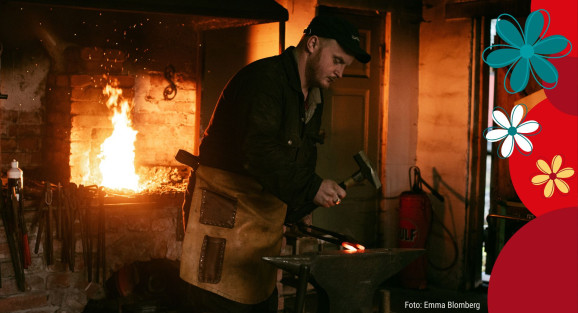 Simon Abrahamsson står i en smedja. Han bär svarta kläder samt ett skinnförkläde. Han står vid ett städ och slår med en hammare på ett glödande järn.Bakom sig brinner det en eld i en ugn.