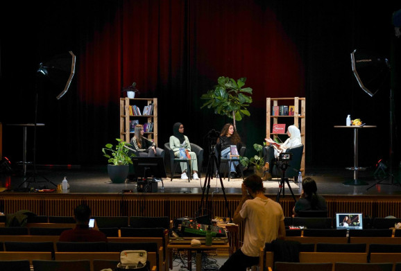 fyra unga kvinnor sitter på en upplyst scen och samtalar