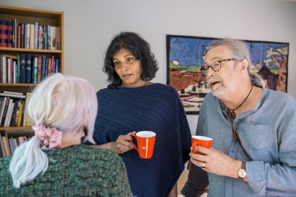 tre personer i samtal, två personer håller kaffe eller tekopp och en person ser man bara bakhuvudet på