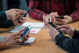 Fyra personer sitter vid bord med mobiltelefoner