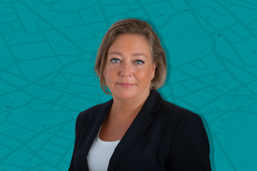 Helen Pettersson tittar in i kameran. Hon bär en svarta kavaj med en vid tröja under. Bakgrunden är turkos