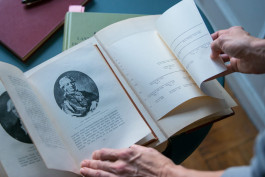 en person har öppnat en bok till vänster syns en gammal målning av ne person på höger ett släktträd