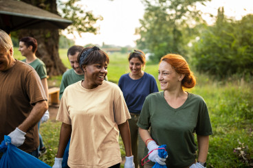 En grupp människor utomhus i sommargrönskande miljö, två kvinnor tittar på varandra i samförstånd och skrattar.