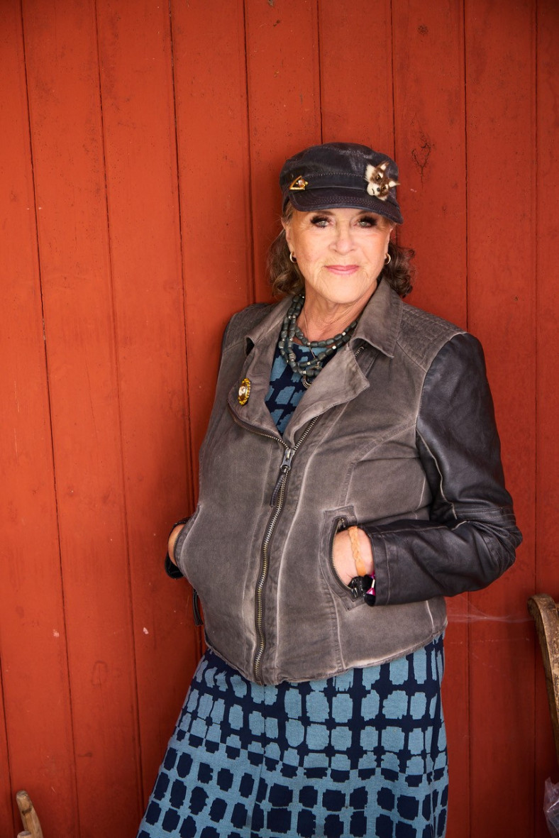 Py står vänd mot kameran med röd trä fasad i bakgrunden