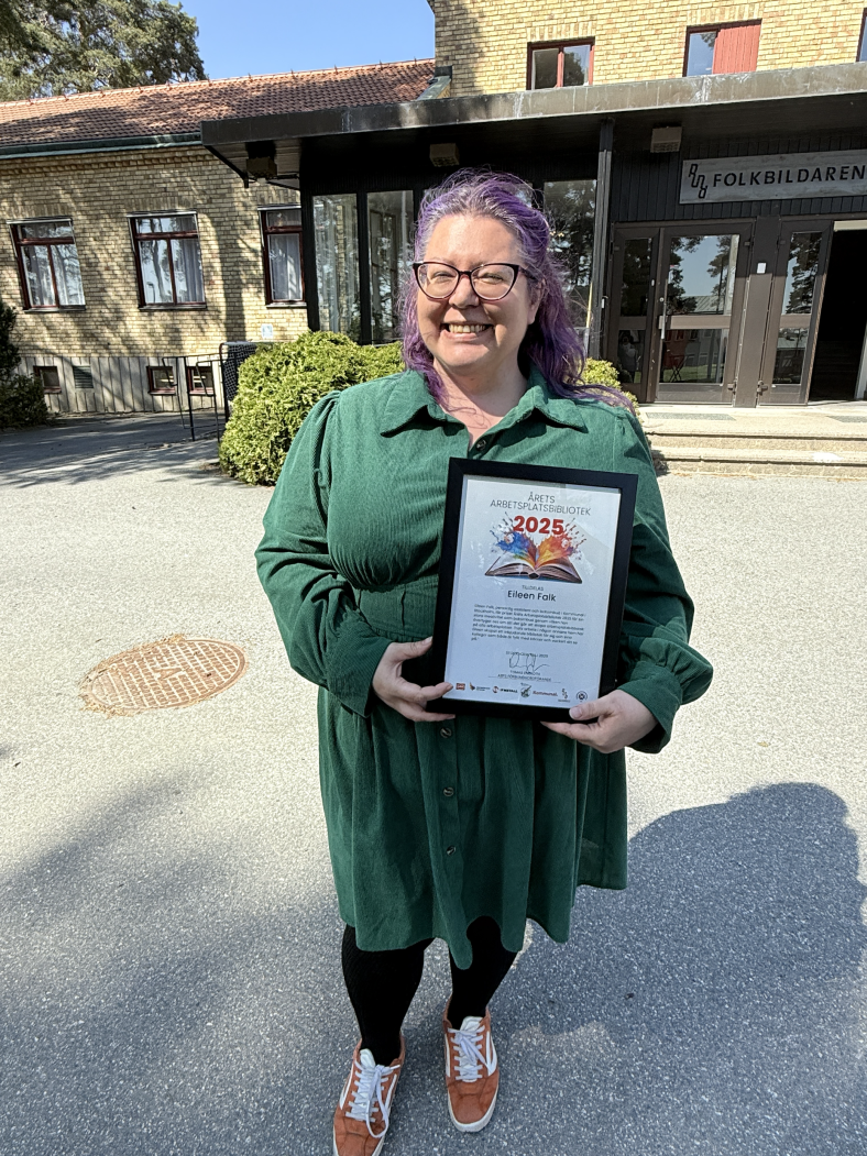 Eileen Falk, vinnare av Boken på arbetsplatsen 2025, håller i sitt diplom utomhus en solig försommardag