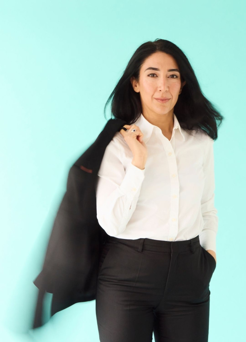 Lawen Redar mot turkos bakgrund. Hon håller kavajen över axeln.