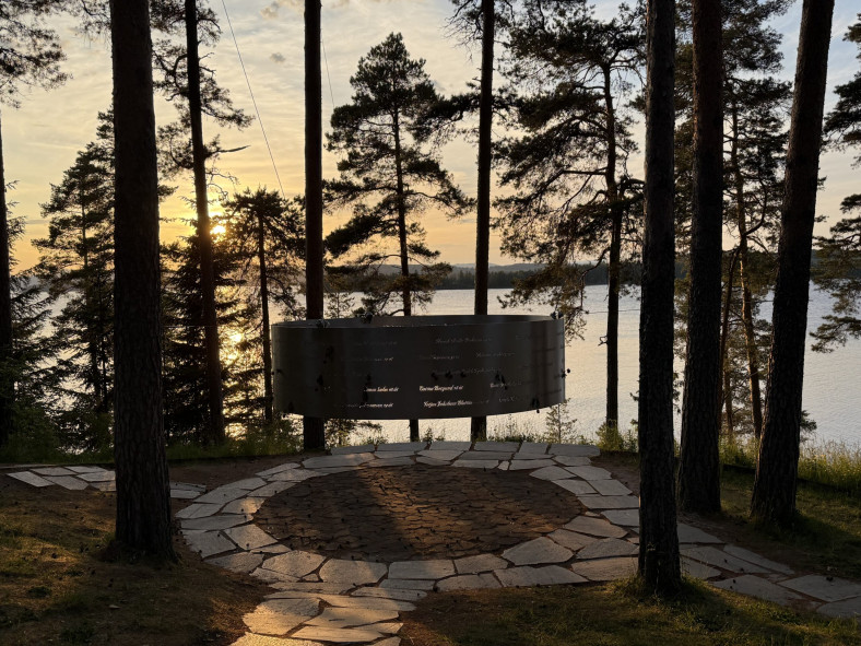 I en skogsglänta i skymningen ser man stor cirkel i stål, i vilken namn och ålder på de 69 som miste livet är utskurna.