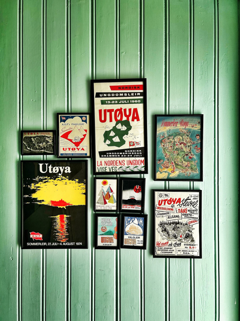 Flera affischer i olika storlekar om olika läger på Utøya genom tiderna sitter på en vägg av grön panel.