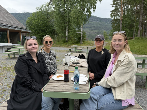 Fyra unga kvinnor sitter vid ett bord utomhus och tittar in i kameran.