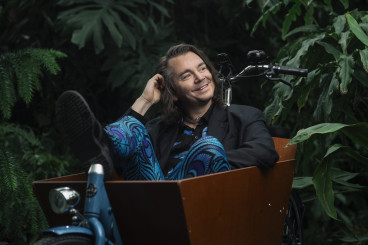 Emil Jensen sitter framför en vägg av gröna växter i en lådcykel, ler och tittar åt sin vänster.