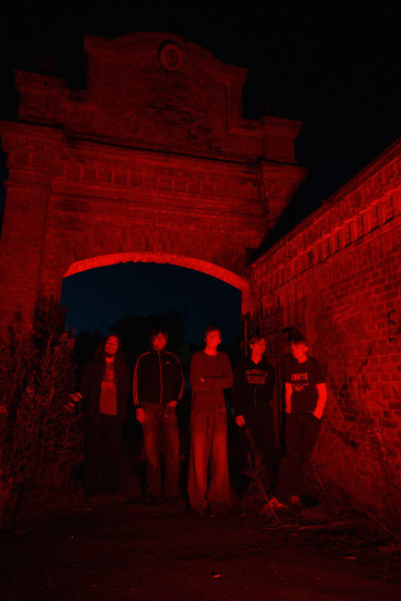 Fem killar står framför en mur. Bilden är mörk och röd.