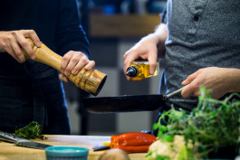 Två personer lagar mat en person pepprar ner i en stekpanna den andra häller i olja