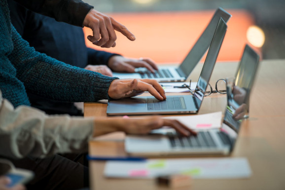 tre laptops på ett bord tre par händer över de tre laptopsen