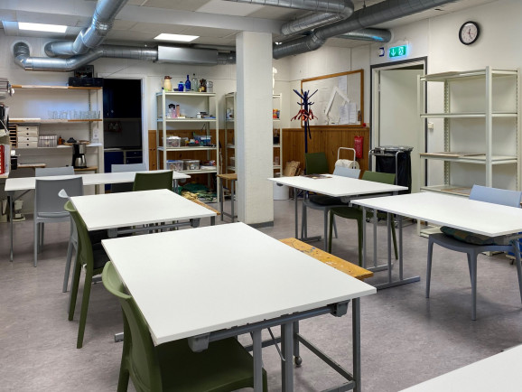 Ett antal vita studiebord står utplacerade i konstsalen på ABFs Hantverksgården i Tyresö, uppställda två och två. Längs väggen står hyllor med konstnärsmaterial som används i kurserna och i mitten av rummet syns en vit pelare.