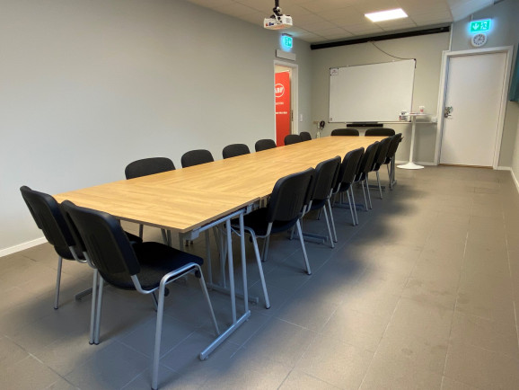 Studierummet Samlingen har ett långt träbord med 12 svarta stolar runt. I bakgrunden, på bortre kortsidan, syns en whiteboard. I dörröppningen en röd roll-up med ABFs logotyp på.