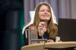 en kvinna står vid talarbord med mikrofon och en dator framför sig