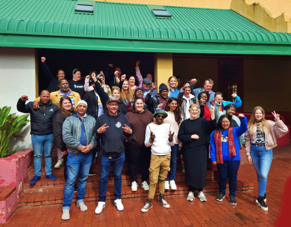 en stor grupp personer ler mot en kamera och vinkar