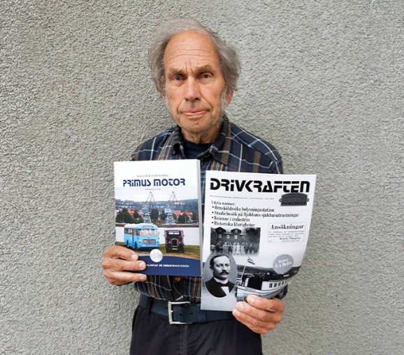 Porträttbild på Börje Göransson som håller upp boken om Primus Motor och tidningen Drivkraften